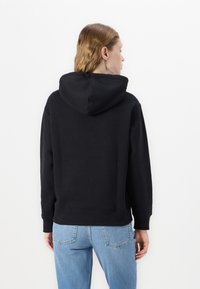 Black hooded sweatshirt with a regular fit, ribbed cuffs, and hem. Styled with light blue jeans and a smooth fabric texture.