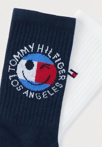 Κάλτσες σε ναυτικό μπλε και λευκό χρώμα με κυκλικό λογότυπο που απεικονίζει ένα χαμογελαστό πρόσωπο, μπλοκ χρωμάτων σε μπλε και κόκκινο και το κείμενο "Tommy Hilfiger Los Angeles". Απαλή υφή.