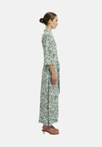 Robe maxi fleurie dans des tons de vert et de bleu, réalisée en tissu léger avec une taille à nouer, des manches trois-quarts et une coupe décontractée.