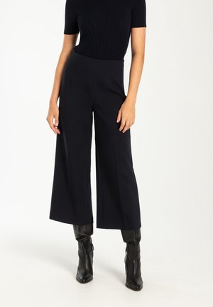 Person wearing black ribbed short-sleeve top, high-waisted wide-leg black pants, and black mid-calf heeled leather boots.