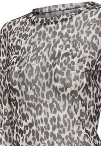 Haut à manches longues avec un motif léopard dans des nuances de gris, noir et beige sur fond blanc.