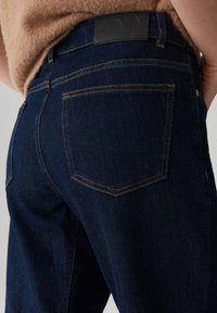 Donkerblauwe denim jeans met een hoge taille, oranje stiksels en een zwart leren label aan de achterkant. Voorzien van twee achterzakken.