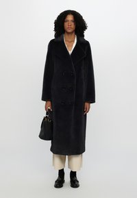Navy long coat with a wool-like texture, double-breasted design, large collar, and six buttons; paired with a black handbag and loafers.
