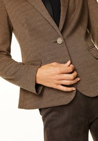 Hnědý kostkovaný blazer s jedním knoflíkem, klopami a bočními kapsami. Textura látky vypadá hladce a upraveně.