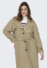 Béžový trench coat s opaskom, zapínaním na gombíky, širokým golierom a dvoma prednými vreckami. Má texturovanú tkaninu a nastaviteľné manžety.