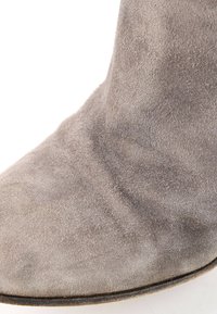 Gros plan du bout d'une botte en daim gris avec texture visible et bord fin de semelle sombre sur fond blanc.