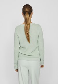 Pull tricoté vert clair avec un motif texturé, poignets et ourlet côtelés. Porté avec un pantalon vert clair assorti, présenté de dos.