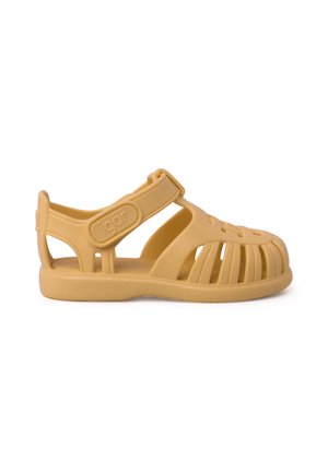 Sandal de goma amarilla con la punta cerrada, lados abiertos, correa alrededor del tobillo y un diseño texturizado y ranurado para ventilación.
