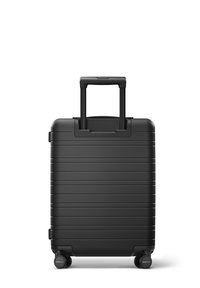 Black hard-shell suitcase with horizontal ridges, telescopic handle, and four wheels for mobility. Smooth texture and compact design.