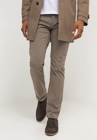 Beige katoenen broek met een slim fit, gestikte details en zijzakken, gedragen met donkerbruin suède schoenen.