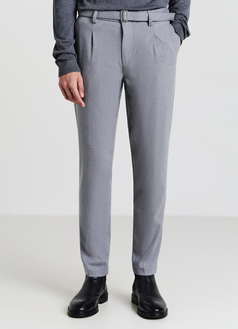 Pantaloni grigi su misura con pince, una texture liscia e una silhouette aderente. Presentano una cintura abbinata e sono abbinati a stivali neri alla caviglia.