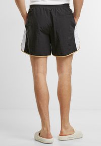 Sorte treningsshorts laget av lett stoff med hvite sidepaneler og gullkant. Har elastisk midjebånd og en baklomme.
