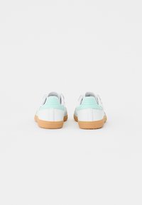 Zapatillas blancas con suaves acentos de menta, parte trasera texturizada y suelas de goma. Diseño redondeado con cuello acolchado, sin hardware visible.