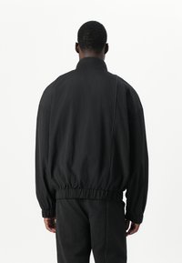 Schwarze Bomberjacke mit elastischen Bündchen und Saum. Verfügt über einen hohen Kragen und eine lockere Passform, hergestellt aus strukturiertem Stoff.