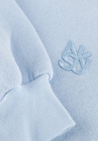 Hellblauer Strickstoff mit geripptem Bündchen und passendem gesticktem abstrakten Logo auf der weichen Stoffoberfläche.