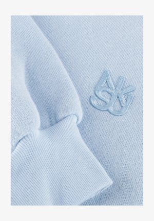 Lichtblauwe gebreide stof met geribde manchet en bijpassend geborduurd abstract logo op de zachte stof van het kledingstuk.