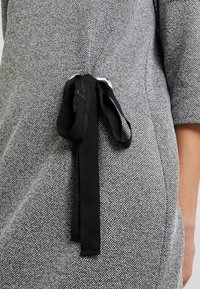 Robe grise tissée avec un motif texturé, dotée d'un lien noir ajustable et d'une quincaillerie argentée à l'arrière pour une silhouette ajustée.