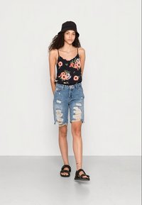 Camisola de alças com padrão floral preto e calções de ganga azul claro desfiados. Um chapéu de balde preto e sandálias pretas completam o visual.