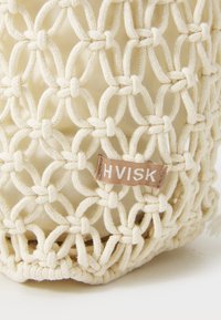 Krämfärgad nätad bomullsväska med mjukt innerfoder och rektangulärt botten. Har en sydd tygskylt med "HVISK" i vitt.