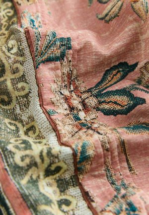Pink fabric with detailed green and beige floral and ornamental patterns, captured in soft folds highlighting texture and stitching.
