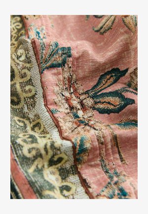 Pink fabric with detailed green and beige floral and ornamental patterns, captured in soft folds highlighting texture and stitching.