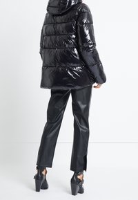 Černá lesklá péřová bunda s kapucí, s horizontálně prošívanými sekcemi. Kombinováno s černými koženými kalhotami a koženými kotníkovými botami na podpatku.