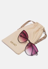 Gafas de sol estilo gato con lentes en degradado rosa-púrpura, acompañadas de un bolso con cordón beige que presenta el logo dorado "LIU JO".