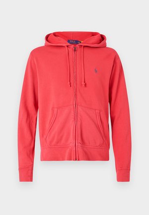 Červená zipsová mikina vyrobená z mäkkej tkaniny, so šnúrkou na kapucni, prednými vreckami a malým logom na hrudi. Hladká textúra a ležérny dizajn.