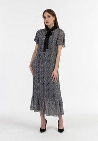 Abito lungo bianco e nero con motivo floreale, maniche corte a sbuffo, orlo rifinito con volant e dettaglio di fiocco nero sul colletto.