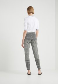 Chemise blanche à manches courtes avec des accents noirs côtelés, associée à un pantalon gris à carreaux présentant une coupe slim et un motif quadrillé subtil.