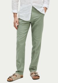 Pantalon en coton vert clair avec une coupe droite, dot�é de poches latérales et d'une texture subtile. Assorti avec des sandales beiges.