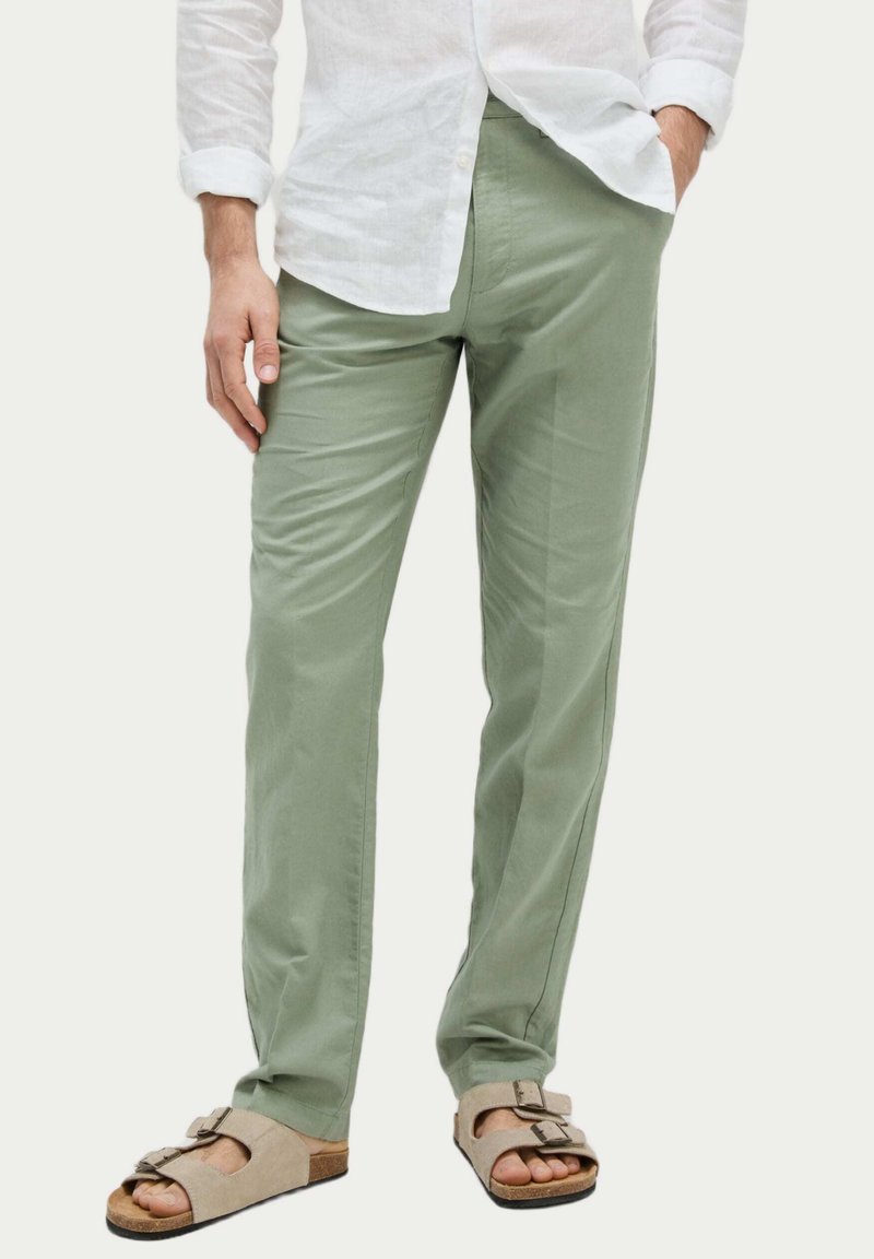 Pantalon en coton vert clair avec une coupe droite, doté de poches latérales et d'une texture subtile. Assorti avec des sandales beiges.