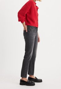 Cárdigan rojo de canalé con botones, jeans rectos grises y mocasines negros con suela gruesa, vistos de lado.