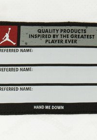 Étiquette en tissu blanche avec un logo Jordan rouge et noir. Le texte indique "PRODUITS DE QUALITÉ INSPIRÉS PAR LE MEILLEUR JOUEUR DE TOUS LES TEMPS" et des lignes pour les noms.