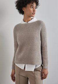 Ljusgrå stickad tröja med en texturerad finish, rund halsringning och långa ärmar, lager på lager över en vit skjorta med krage.