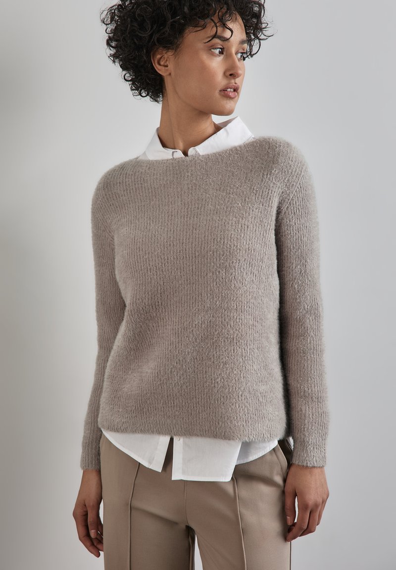 Ljusgrå stickad tröja med en texturerad finish, rund halsringning och långa ärmar, lager på lager över en vit skjorta med krage.