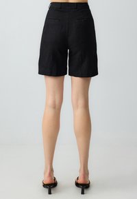 Shorts in lino neri con una vestibilità morbida, lunghezza a metà coscia e due tasche posteriori. Tessuto liscio e design pulito senza marchi visibili.