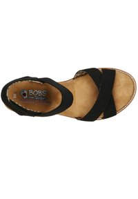 Zwarte stoffen sandaal met kruislings banden, inlegzool van geheugenfoam en een tan kleurige voetbed. Verzorgde hak biedt comfort tijdens het dragen.