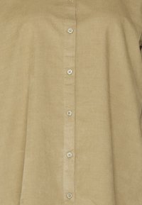 Camisa de pana beige claro con botones en la parte delantera, textura suave y patrón de rayas verticales, con cinco botones a juego.
