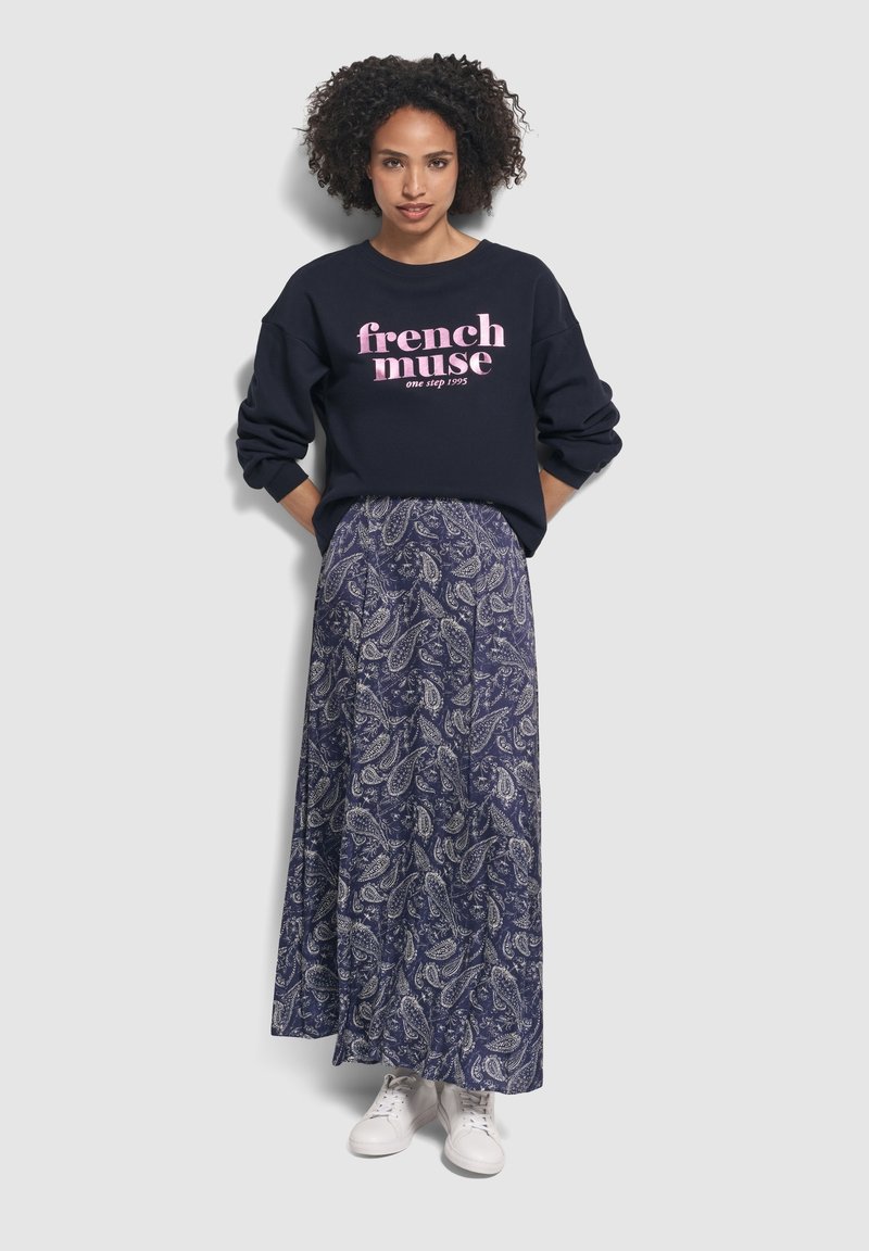 Felpa blu marina con testo rosa "french muse", abbinata a una lunga gonna blu con motivo paisley e sneakers bianche. Look casual, vestibilità rilassata.