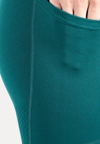 Turquoise sportlegging gemaakt van rekbare, gestructureerde stof. Voorzien van een zijzak en naaddetails. Ademend meshpatroon bij de zoom.