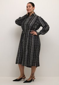 Abito midi a pois in bianco e nero con colletto e maniche a sbuffo, caratterizzato da una vita aderente e una silhouette fluida.