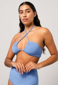 Ljusblå bikiniöverdel med korsande remmar och rynkdetaljer. Slät textur och en stödjande, strukturerad form. Högmidjade matchande underdel.