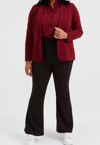 Burgundy blazer over a matching blouse, paired with brown flared pants featuring a subtle pattern. Model wears white sneakers.