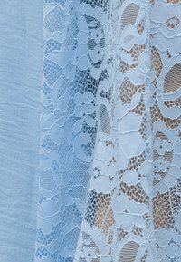 Μπλε ύφασμα με διαφανές λευκό δαντελένιο επικάλυμμα που παρουσιάζει floral μοτίβα και διάφορα υφασμένα σχέδια από δίχτυ.