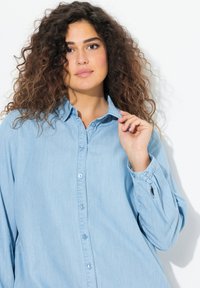 Camicia di jeans azzurro chiaro con chiusura a bottoni, maniche lunghe e vestibilità rilassata. Presenta un colletto classico e una trama sottile.