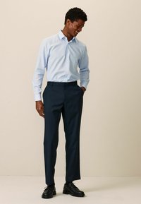Himmelblaues Hemd mit langen Ärmeln, kombiniert mit dunkeln marineblauen Hosen und schwarzen Schuhen. Glattes Material und gerades Bein.