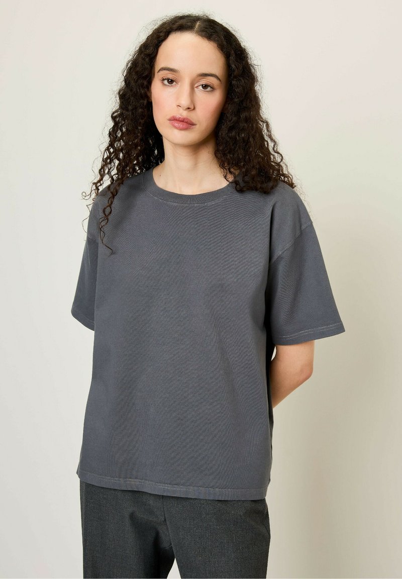 Siv bela majica iz bombaža s okroglim izrezom in kratkimi rokavi, ki ima sproščen kroj in vidne šive.