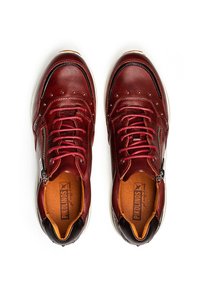 Un par de zapatillas de cuero rojas con cordones y cremalleras laterales, vistas desde arriba, con plantillas marrones y suelas blancas.