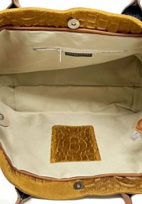 Interiér hnědého a béžového semišového kabelky s hladkým tkaninovým podšívkou, zipovou kapsou a texturovanou koženou akcentovou částí.